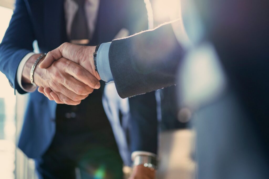 Two professionals in business suits shake hands during a meeting in a modern office, representing partnership, collaboration, or a completed deal