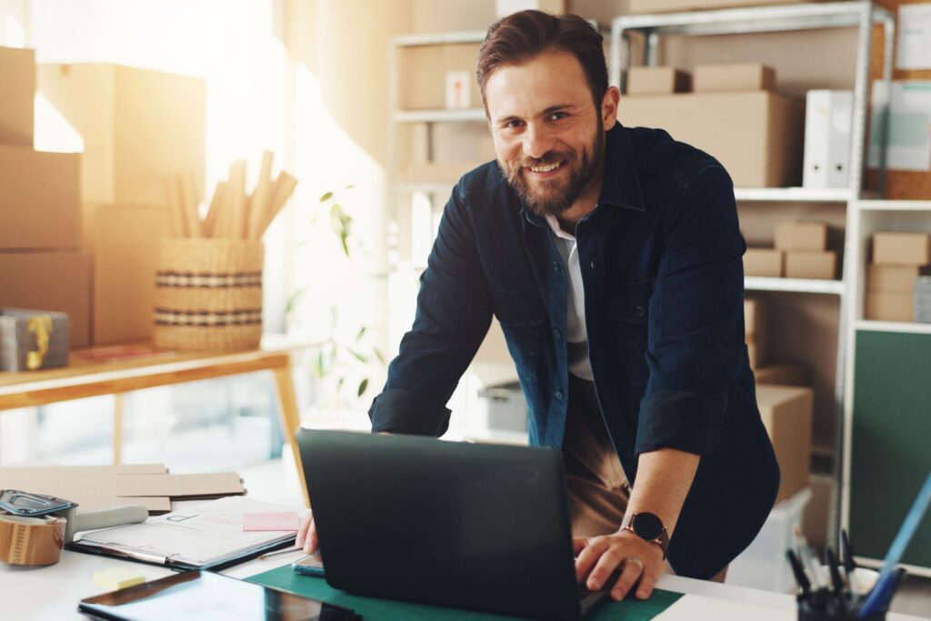 Person sitting at a desk, looking at a clipboard while working on a laptop