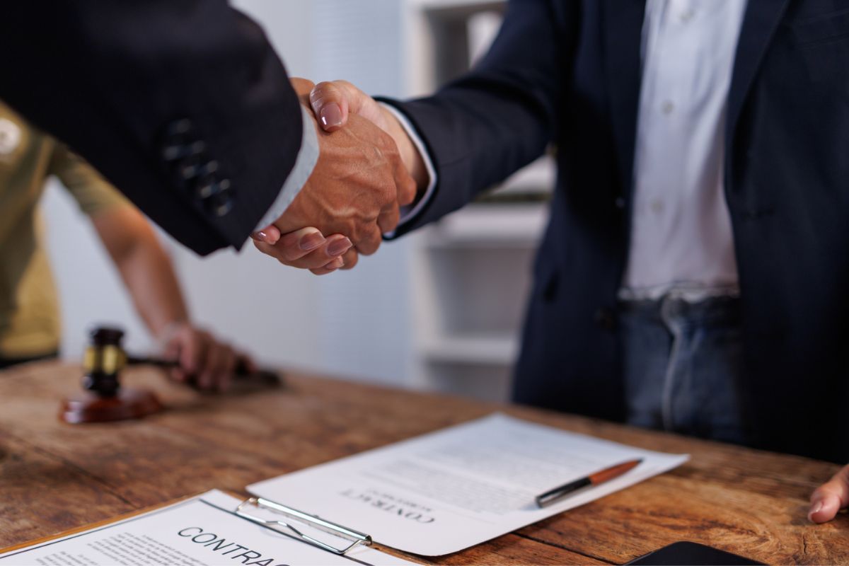 Two business professionals shaking hands over a signed contract, representing a completed agreement or business transaction