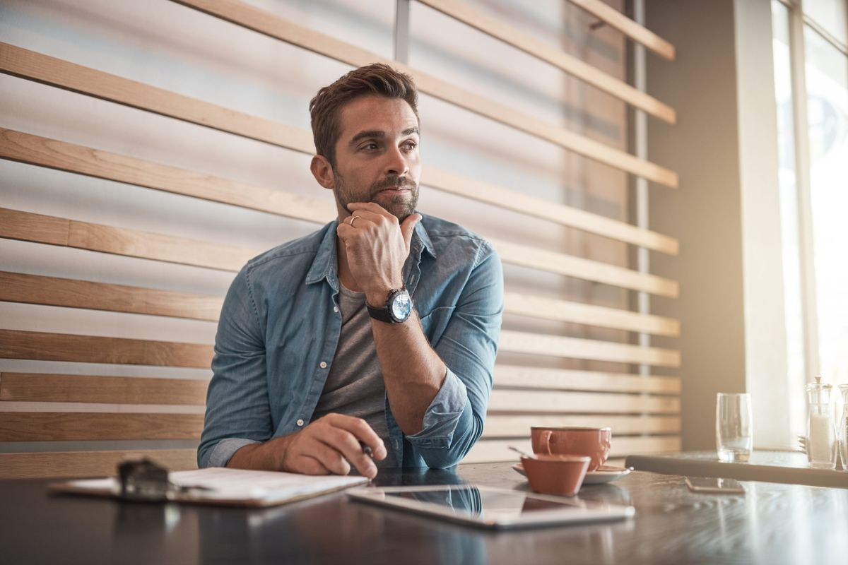 Business owner reviewing documents and thinking at a table with a tablet and coffee