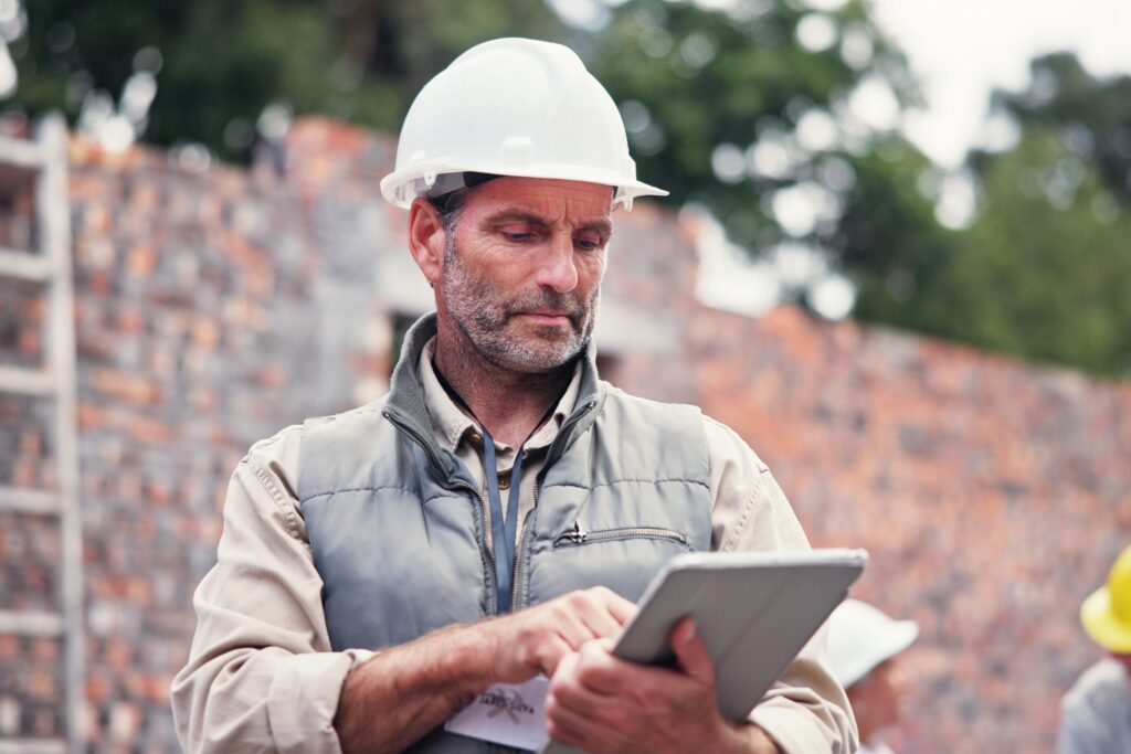 Construction contractor wearing a white hard hat reviewing paperwork outdoors.