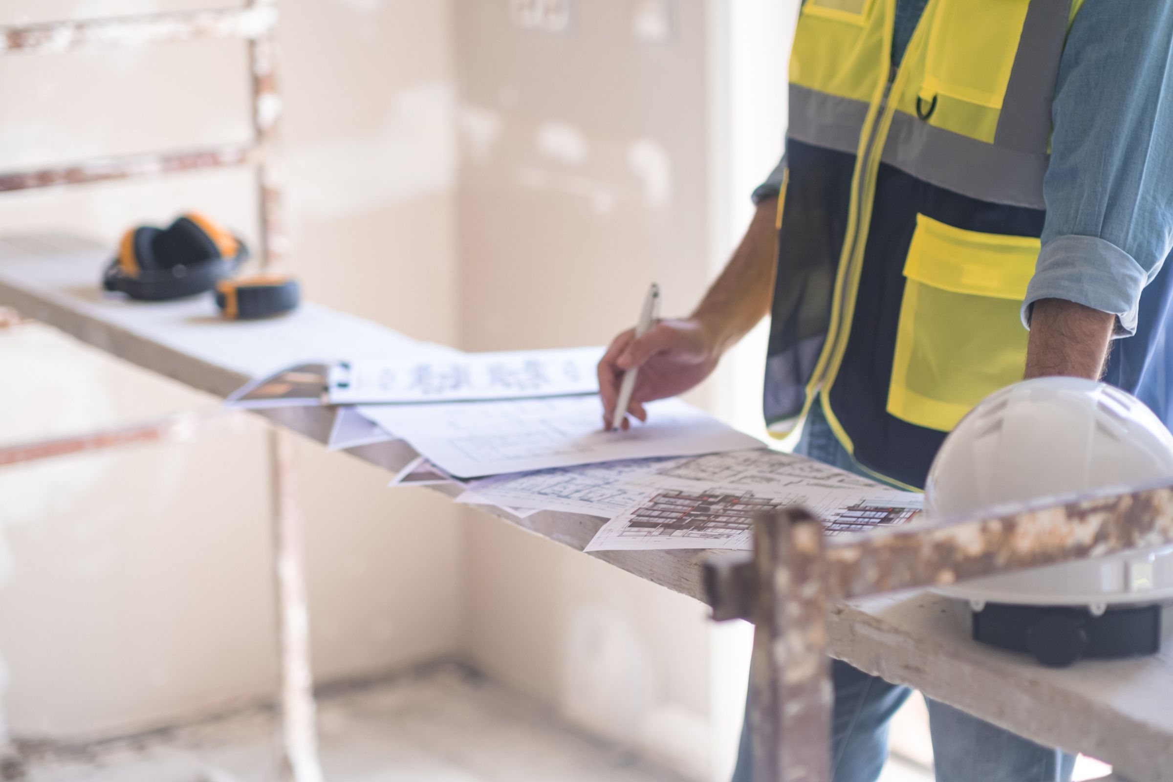 Contractor in a safety vest reviewing construction plans at a worksite.